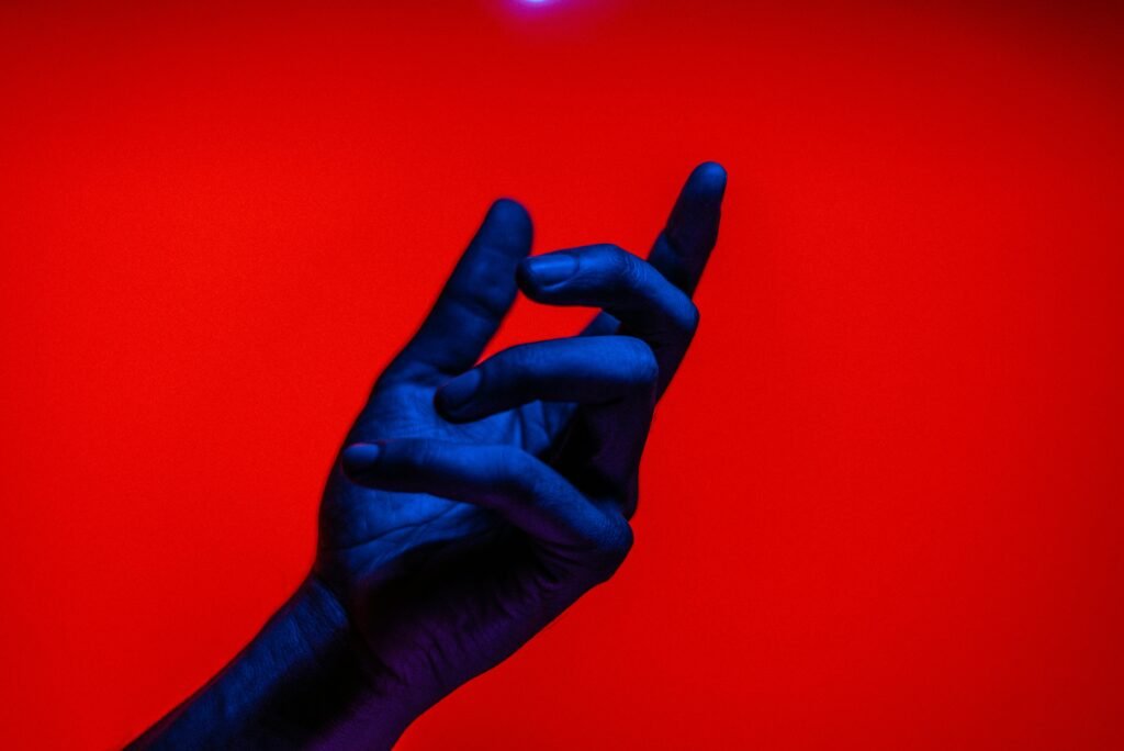 A blue-tinted hand gesturing against a vivid red backdrop, conveying bold conceptual art.