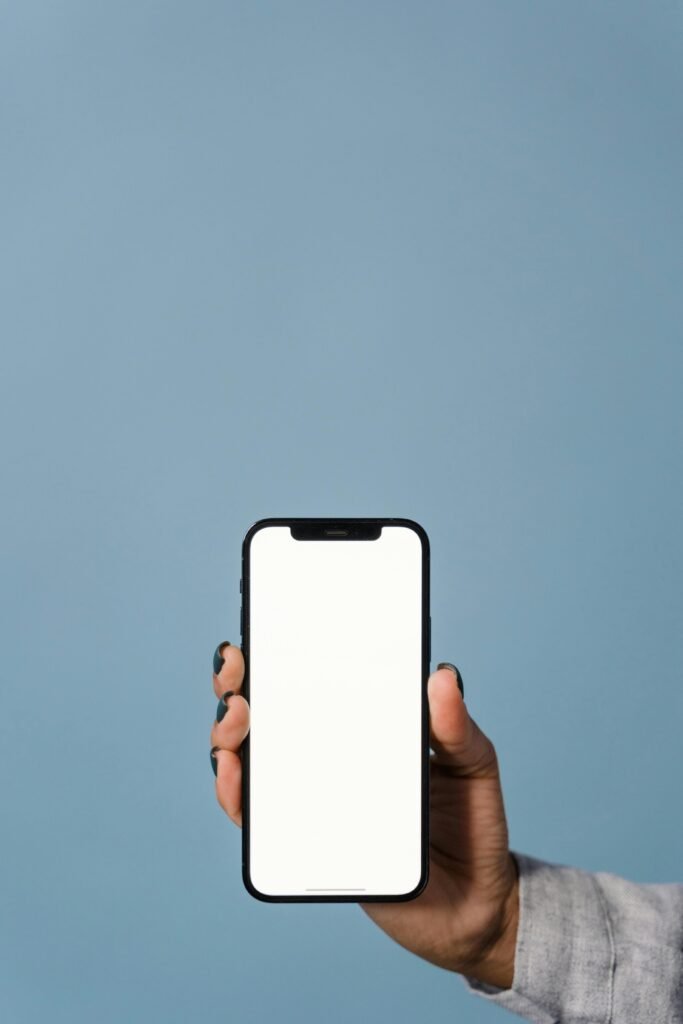 Close-up of a hand holding a smartphone against a blue background, showcasing blank screen.